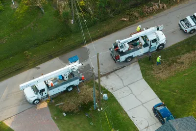 Professional bucket trucks performing overhead power line maintenance in a residential area.