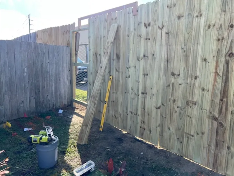 Professional wood fence gate installation with leveler tool and construction equipment.