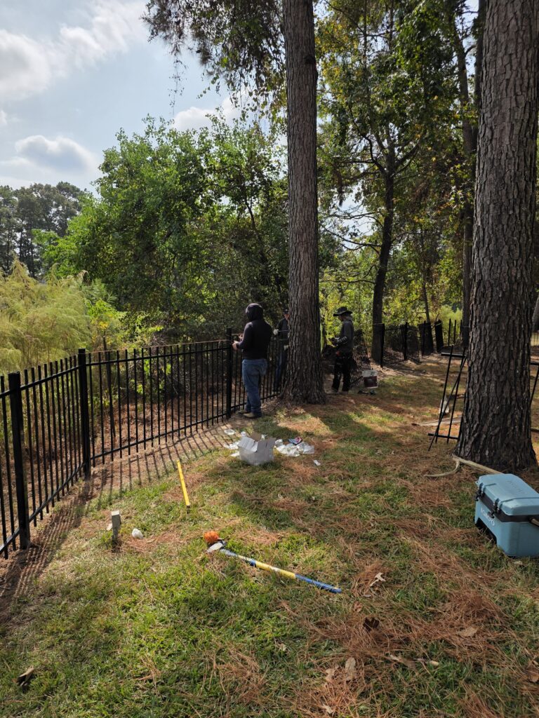 Professional team installing a black metal fence in a wooded backyard.