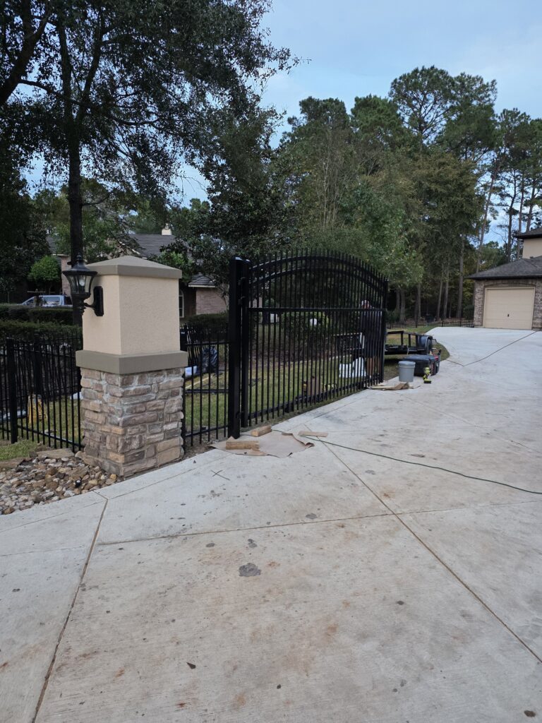 Black ornamental iron fence and stone pillar with lighting.