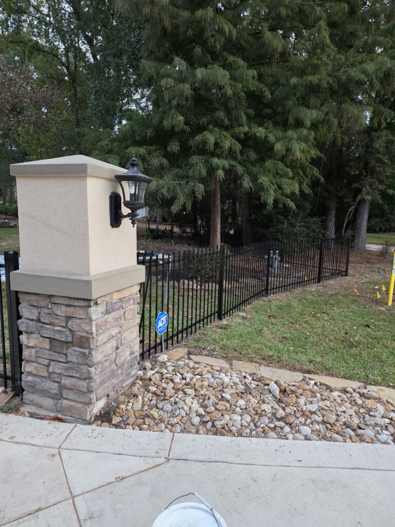 Black metal picket fence with a decorative stone pillar and lamp.