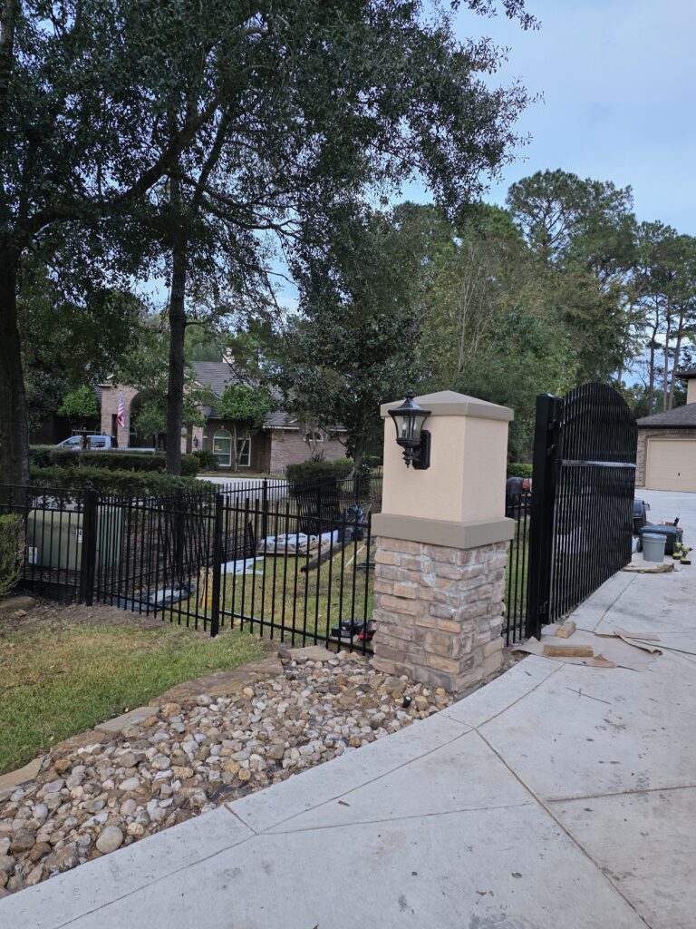 Black ornamental iron fence and stone pillar with lighting.