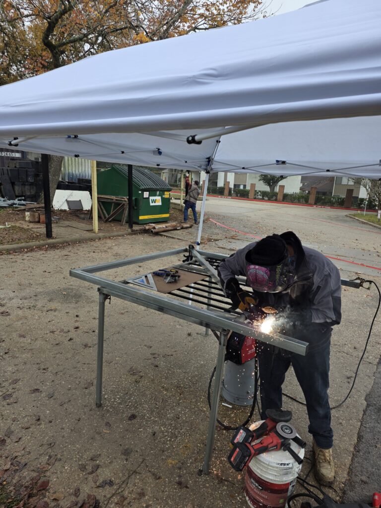 Professional welder fabricating a custom metal gate under a canopy