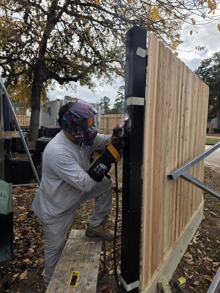 Welder working on a custom wood and metal fence.