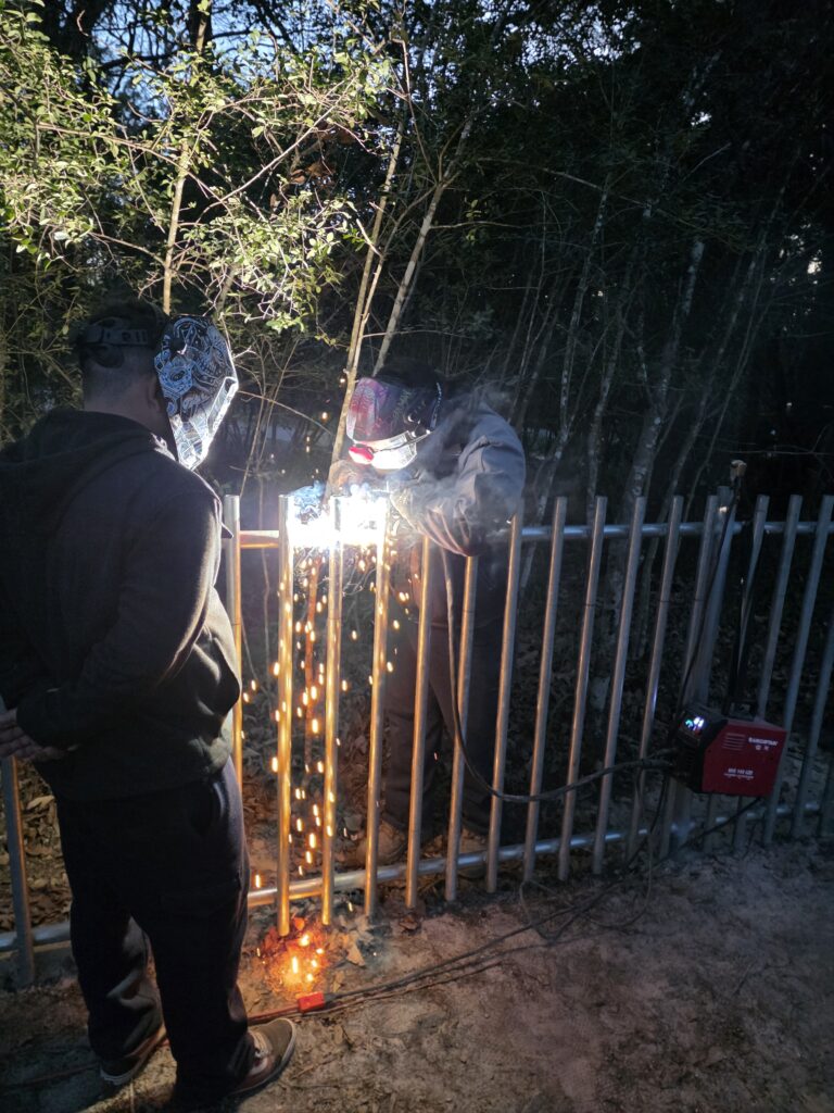 Professional fence contractors welding and repairing a metal security fence at night.