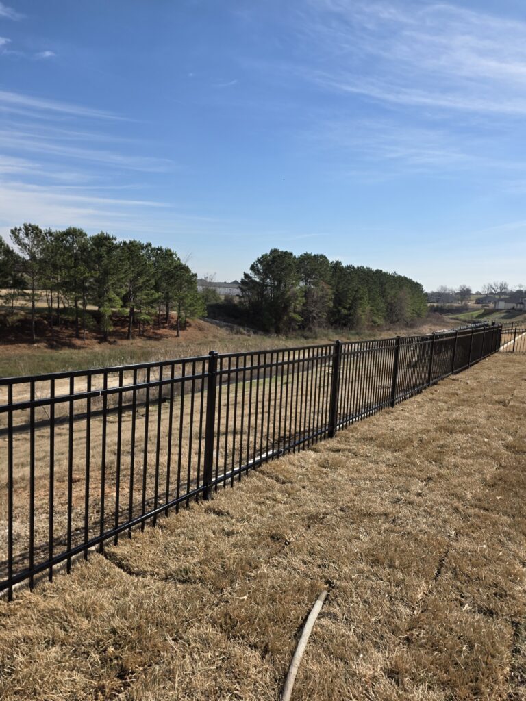 Long black aluminum picket fence across a dry grass field.