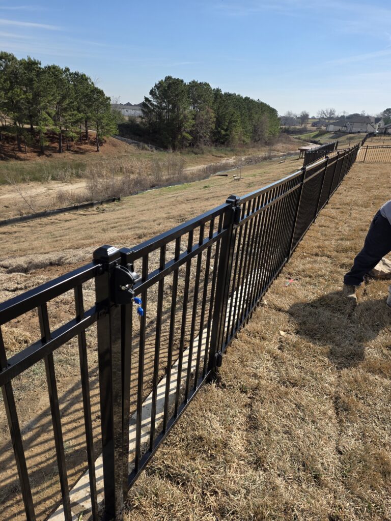 Black aluminum picket fence gate with a secure latch overlooking a field.