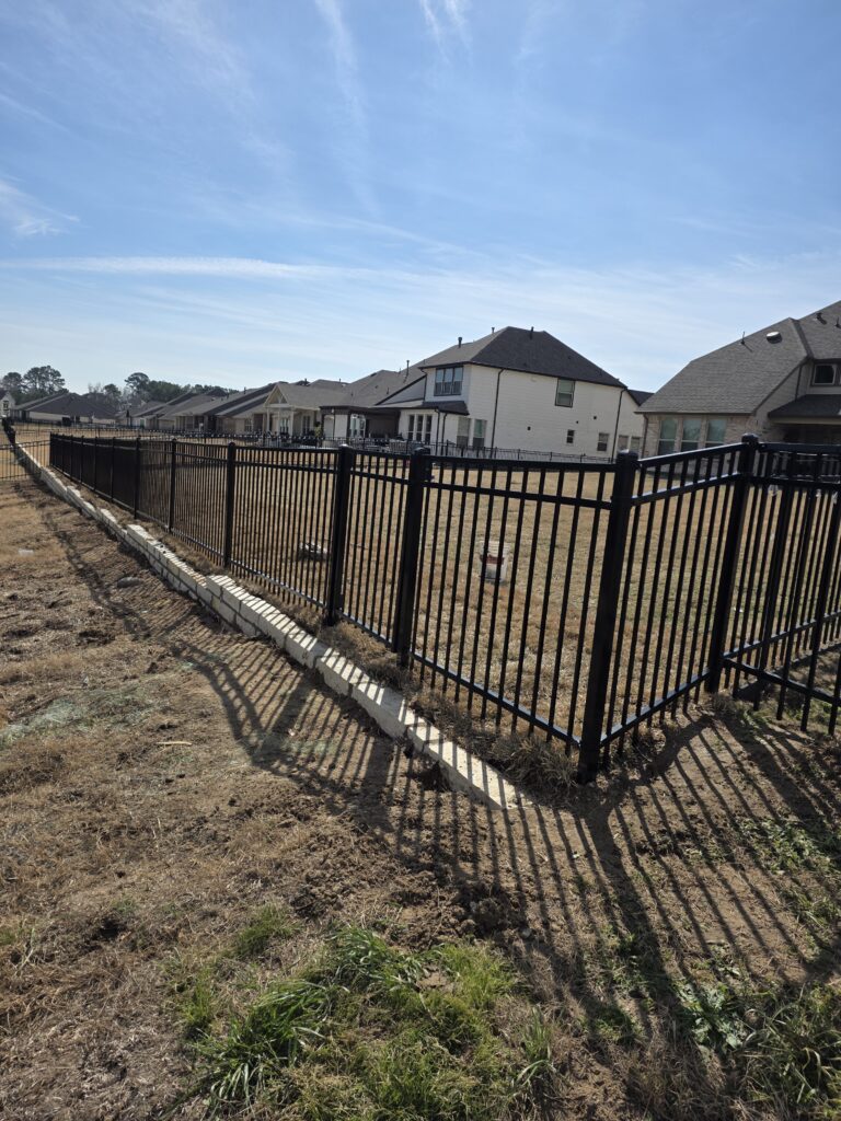 Long black metal picket fence with a concrete base in a residential neighborhood.