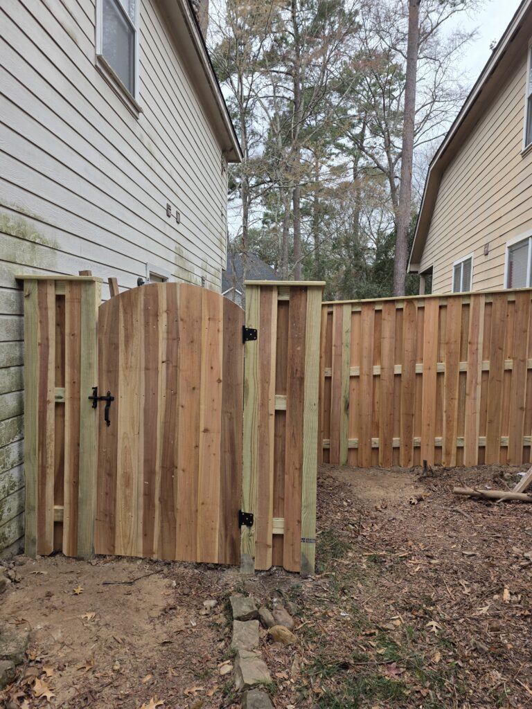 Arched cedar wood gate and matching privacy fence in a residential side yard.
