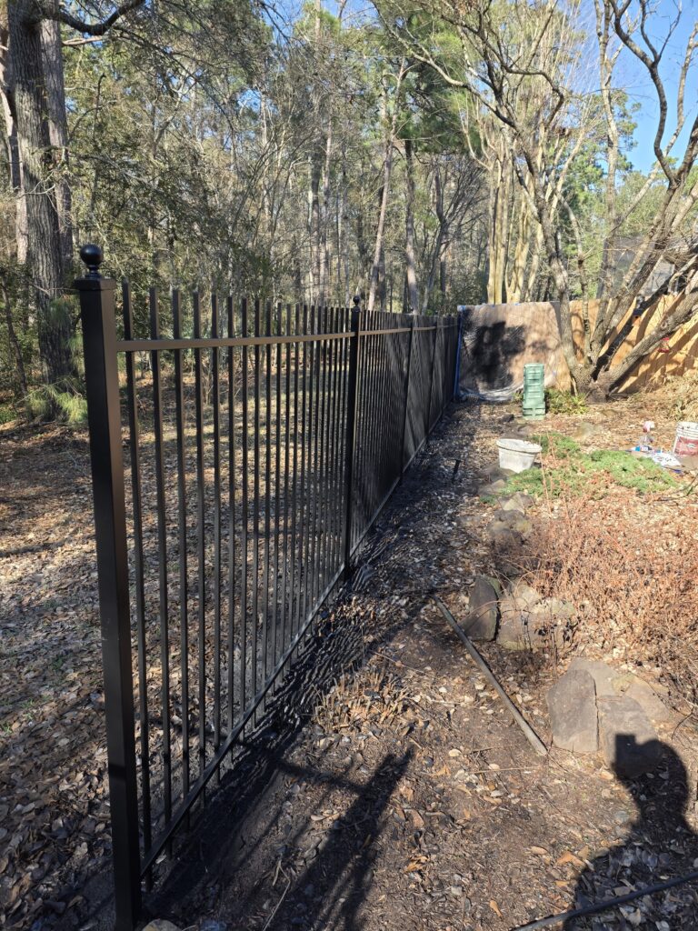 Black metal fence with decorative caps in a garden.