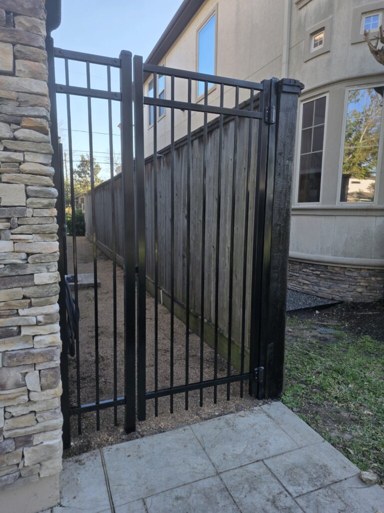 Black metal pedestrian gate installed next to a stone wall